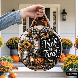 Könnte beinhalten: Ein rundes Holzschild mit dem Schriftzug Trick or Treat in weißer Schreibschrift. Das Design zeigt eine schwarz-weiß karierte Schleife, Sonnenblumen, eine Milchkanne aus Metall, eine leuchtende Laterne, einen Hexenhut und einen Kürbis.