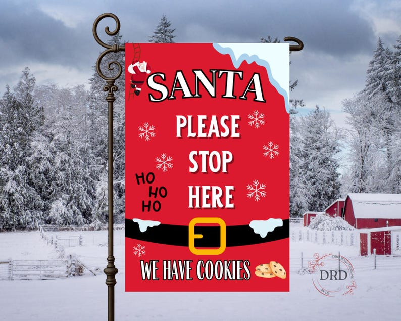 May include: A red Christmas garden flag with the words "SANTA PLEASE STOP HERE" in white. The flag features a Santa belt design with snowflakes and the phrase "WE HAVE COOKIES". A decorative flag for the holiday season.