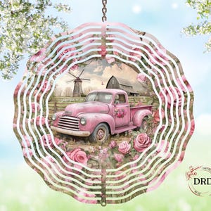 May include: A pink metal wind spinner featuring a vintage pickup truck surrounded by roses. The truck is parked in a field with a barn and windmill in the background. The spinner has a wavy, layered design with a chain for hanging.