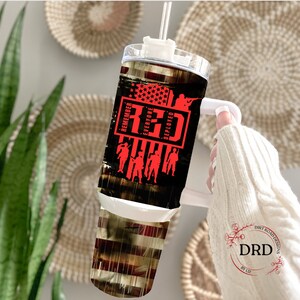 May include: A stainless steel tumbler with a black and red design. The tumbler features a red, white, and blue American flag with the words "Remember Everyone Deployed" and "RED" in red text. The tumbler has a white lid and a white handle.