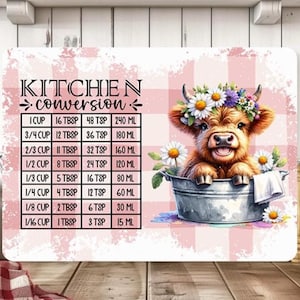 May include: A decorative kitchen conversion chart featuring a watercolor illustration of a Highland cow wearing a flower crown. The chart includes measurements for cups, tablespoons, teaspoons, and milliliters. The background has a pink gingham pattern.