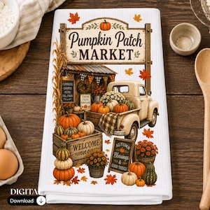 May include: A white waffle-weave kitchen towel featuring a graphic of a vintage truck loaded with pumpkins and fall flowers. The design includes a sign reading Pumpkin Patch Market, a crate labeled Welcome, and an autumn-themed chalkboard sign.