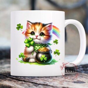 May include: White ceramic mug with a colorful illustration of a cat holding a pot of gold and a shamrock. The cat has orange, black, and white fur. The background includes green shamrocks and a rainbow.