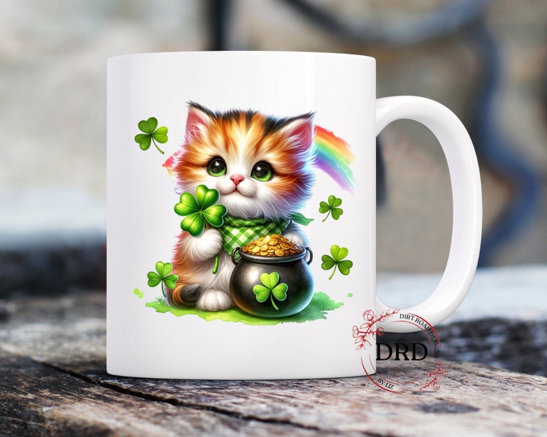May include: White ceramic mug with a colorful illustration of a cat holding a pot of gold and a shamrock. The cat has orange, black, and white fur. The background includes green shamrocks and a rainbow.