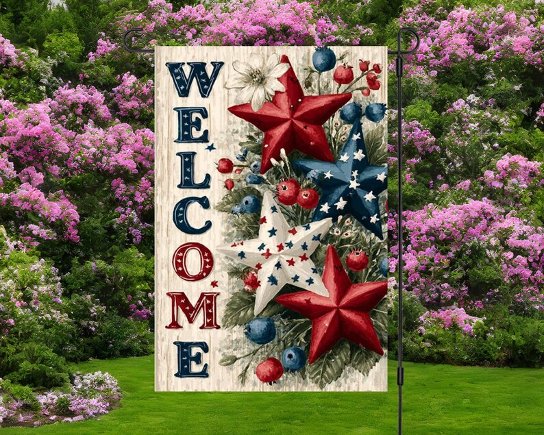 Pu&ograve; includere: Una bandiera da giardino con la scritta "WELCOME" in lettere rosse, bianche e blu. La bandiera presenta stelle rosse, bianche e blu, bacche e accenti floreali. La bandiera &egrave; esposta su un supporto in metallo nero in un giardino.