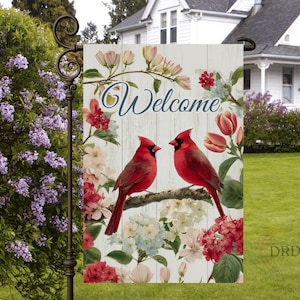 May include: A garden flag with a floral and bird design. The flag features two red cardinals perched on a branch, surrounded by flowers and the word "Welcome" in script. The background has a white wood plank design.