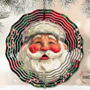 Puede incluir: Un adorno navide&ntilde;o circular y en capas con Santa Claus. El adorno tiene un borde con estampado rojo y verde con la cara sonriente de Santa en el centro, con barba blanca, sombrero y gafas rojas. El adorno cuelga de una cadena plateada.