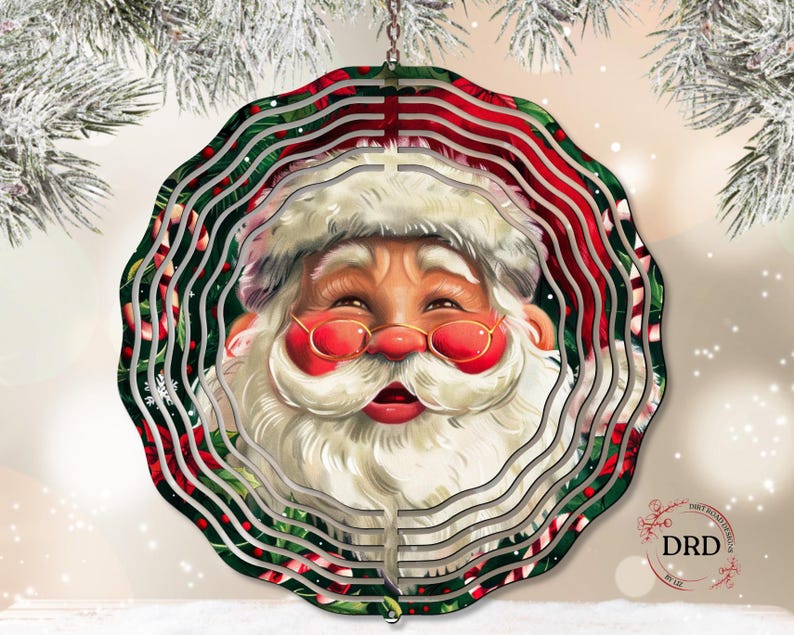 Puede incluir: Un adorno navide&ntilde;o circular y en capas con Santa Claus. El adorno tiene un borde con estampado rojo y verde con la cara sonriente de Santa en el centro, con barba blanca, sombrero y gafas rojas. El adorno cuelga de una cadena plateada.
