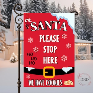 May include: A red Christmas garden flag with the words "SANTA PLEASE STOP HERE" in white. The flag features a Santa belt design with a gold buckle, snowflakes, and the text "WE HAVE COOKIES". A decorative garden stake holds the flag.