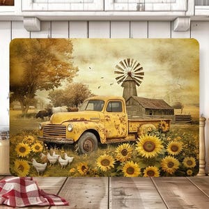 May include: A rectangular cutting board featuring a vintage yellow truck parked in a field of sunflowers. A windmill and farmhouse are in the background. Chickens are in the foreground. The overall color palette is warm, with sepia tones.