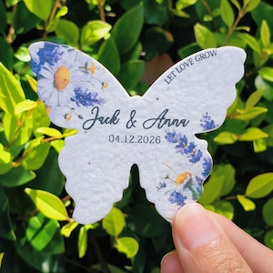 May include: A butterfly-shaped seed paper with blue, yellow, and white floral patterns. The text "Jack & Anna" and the date "04.12.2026" are printed on the front. The words "LET LOVE GROW" are printed on the top wing.