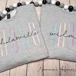 Puede incluir: Dos sudaderas grises con números y texto bordados. La sudadera de la izquierda tiene el número 4036 y el texto "nicholasville". La sudadera de la derecha tiene el número 4030 y el texto "wilmore".