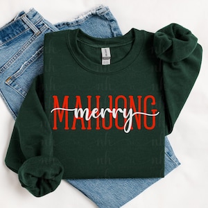 May include: A dark green sweatshirt with the words "MAHJONG merry" in red and white lettering. The sweatshirt is folded on top of a pair of blue jeans. The sleeves are rolled up.