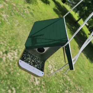 May include: A green bird feeder with a white plastic base and a clear plastic window. The feeder is hanging from a white rope and is filled with birdseed.