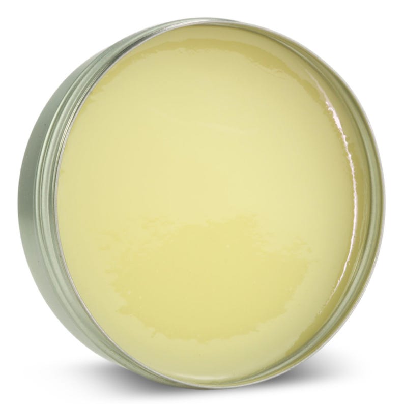 Puede incluir: Un recipiente redondo de hojalata lleno de un b&aacute;lsamo o ung&uuml;ento de color amarillo p&aacute;lido.