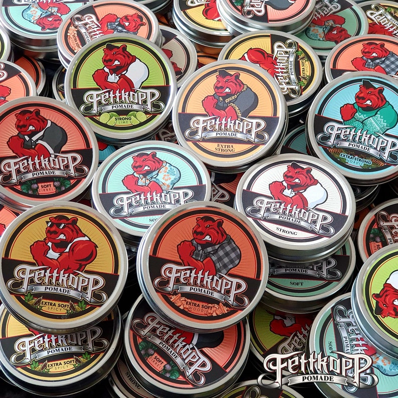 Puede incluir: Una colecci&oacute;n de recipientes redondos de varios tama&ntilde;os con tapas, todos con el mismo nombre de marca "Fettkopp" y la palabra "Pomade". Cada recipiente tiene un dise&ntilde;o diferente con un personaje de dibujos animados y un texto que describe el tipo de pomada que contiene, como "Extra Soft Spicy" y "Strong".