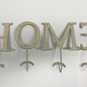 Puede incluir: Letrero HOME de metal blanco con ganchos. Cada letra es un gancho separado.