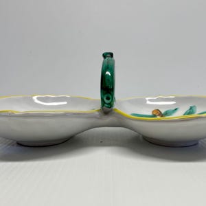 Puede incluir: Un plato de servir de cer&aacute;mica blanca con dos secciones y un asa verde. El plato tiene un borde amarillo y est&aacute; decorado con dise&ntilde;os florales verdes y amarillos.