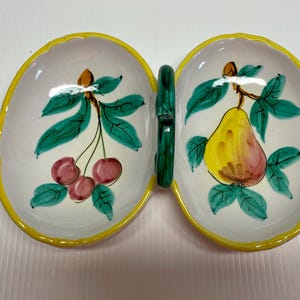 Puede incluir: Un plato de servir de cer&aacute;mica blanca con un borde amarillo y un asa verde. El plato est&aacute; dividido en dos secciones, cada una con un dise&ntilde;o de fruta diferente. Una secci&oacute;n tiene una pera con hojas verdes, mientras que la otra secci&oacute;n tiene cerezas con hojas verdes.