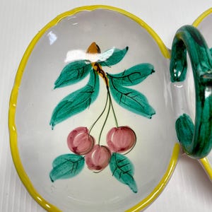 Puede incluir: Un plato de servir de cer&aacute;mica blanca con un borde amarillo y un dise&ntilde;o pintado a mano de cerezas y hojas. El plato tiene dos secciones y un asa verde.