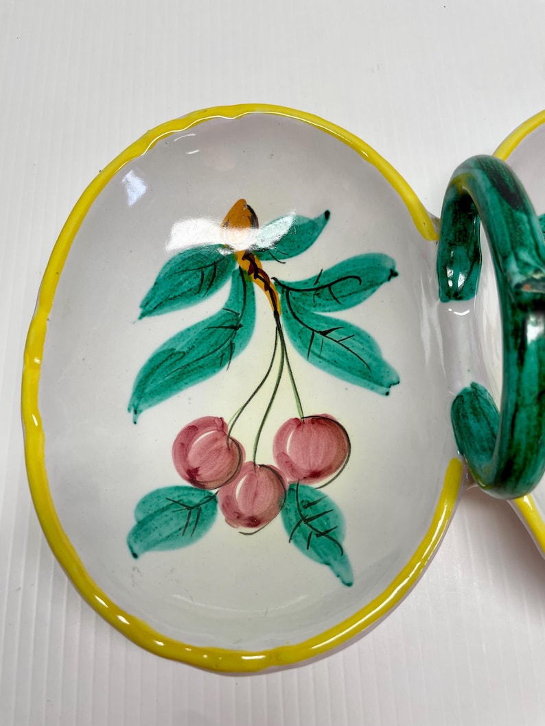 Puede incluir: Un plato de servir de cer&aacute;mica blanca con un borde amarillo y un dise&ntilde;o pintado a mano de cerezas y hojas. El plato tiene dos secciones y un asa verde.