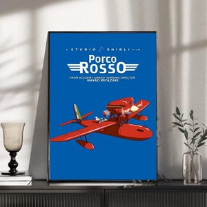 Op de afbeelding: Een ingelijste poster van de animatiefilm "Porco Rosso" van Studio Ghibli. De poster toont een rood watervliegtuig tegen een blauwe achtergrond, met de titel van de film in het wit. De tekst "FROM ACADEMY AWARD-WINNING DIRECTOR HAYAO MIYAZAKI" is ook opgenomen.