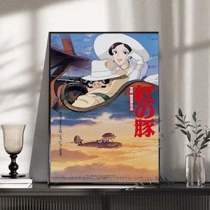 May include: Framed poster featuring a vibrant illustration from the animated film "Porco Rosso." The artwork depicts a pig-like character in a biplane, with a woman in a white hat. Japanese text is visible. The background shows a sunset sky.
