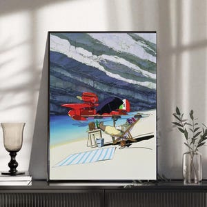 May include: Framed art print featuring a vibrant illustration of a red seaplane on the water near a beach. A person relaxes in a beach chair, with a striped towel and small table nearby. The background shows a rocky cliff and blue water.