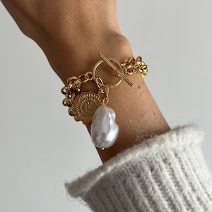May include: A gold chain bracelet with a large pearl charm and a gold coin charm. The bracelet has a toggle clasp.