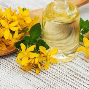 May include: A glass bottle of clear yellow St. John's Wort oil with yellow flowers on a wooden surface.