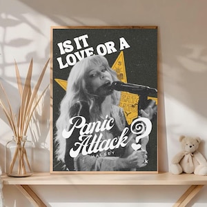 Puede incluir: Un póster en blanco y negro enmarcado que presenta a una cantante con cabello largo sosteniendo un micrófono. El póster tiene el texto "IS IT LOVE OR A Panic Attack?" con el nombre de la artista, Halsey, debajo.