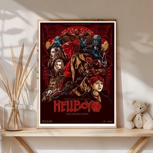 May include: A framed poster featuring the movie "Hellboy: The Golden Army." The artwork showcases a dark red background with various characters in shades of red, blue, and tan. The title "Hellboy" is prominently displayed in red.