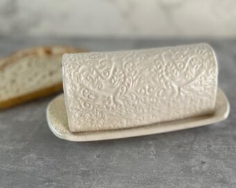 May include: White ceramic butter dish with a decorative floral pattern. The dish has a lid and a base.
