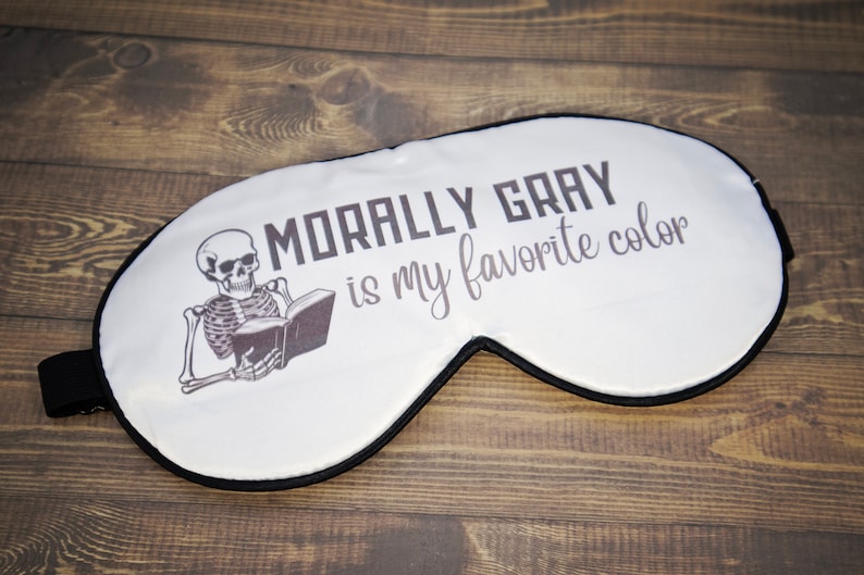 K&ouml;nnte beinhalten: Wei&szlig;e Schlafmaske mit einem schwarzen Skelett, das ein Buch liest, und dem Text "Morally Gray is my favorite color".