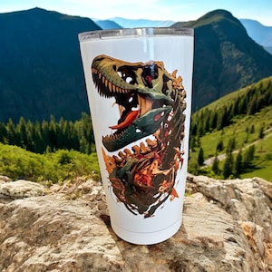 Puede incluir: Vaso térmico blanco con una ilustración detallada de un esqueleto de dinosaurio. El diseño presenta una boca abierta y una lengua roja, con tonos marrones, verdes y rojos. El vaso es cilíndrico y tiene una tapa transparente.