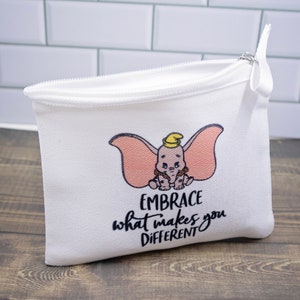 May include: White zippered pouch with a pink and grey cartoon elephant with a yellow hat. The pouch has the text "EMBRACE what makes you DIFFERENT" printed on it.