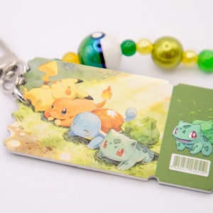 May include: A rectangular keychain shaped like a ticket featuring a colorful illustration of Pikachu, Charmander, Squirtle, and Bulbasaur. A green section on the right shows Bulbasaur and a barcode. It includes a silver clasp and green and yellow beads.