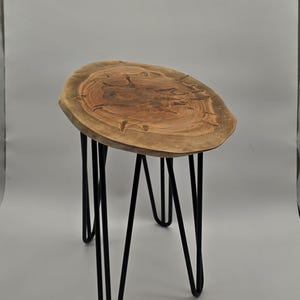 May include: A side table featuring a natural, irregular-shaped wooden slab top with visible grain and a dark, carved star-like pattern in the centre. The tabletop is supported by four slender, black metal hairpin legs that angle outward.