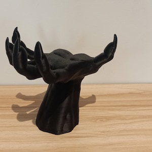 Könnte beinhalten: Eine schwarze Skulptur zweier offener Hände, Handflächen nach oben, mit strukturierter Oberfläche. Die Hände sind mit einem Sockel verbunden. Die Skulptur steht vor einem neutralen Hintergrund.
