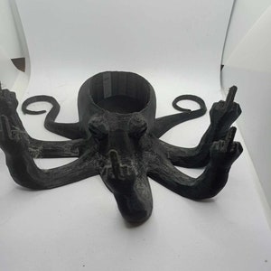 May include: A black 3D-printed octopus-shaped container with a round opening. Each of the eight tentacles is raised, with the middle finger extended. The container is on a white surface.