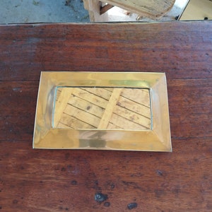 Puede incluir: Un pequeño espejo rectangular con marco de latón que refleja una superficie de madera.