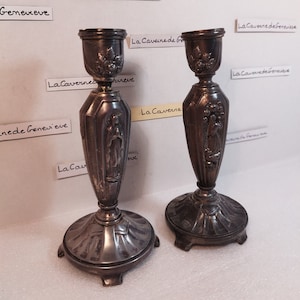 Puede incluir: Dos candelabros de plata con un diseño de figura religiosa. Los candelabros tienen una base redonda con tres patas y un cuerpo alto y delgado.