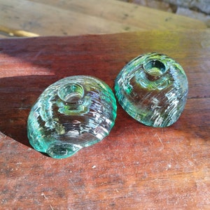 Peut inclure: Deux bougeoirs en verre vert turquoise avec une surface texturée. Les bougeoirs sont en forme de dôme avec un petit trou au centre pour une bougie.