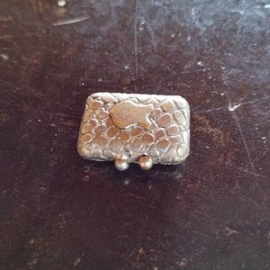May include: A small silver box with a textured surface and a gold fish design on the top. The box has two small silver hinges.