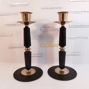 May include: Two black and gold candle holders with a round base and a tall, cylindrical design. The candle holders have a gold top and a gold band around the middle.