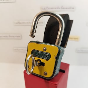 May include: A yellow and green padlock with a key inserted in the keyhole. The padlock has the word "ABUS" printed on the front.