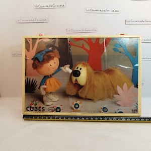 May include: A vintage wooden box with a colorful illustration of a girl and a dog. The box is labeled "Roule Cubes" and has a red and blue design. The box is made in France.