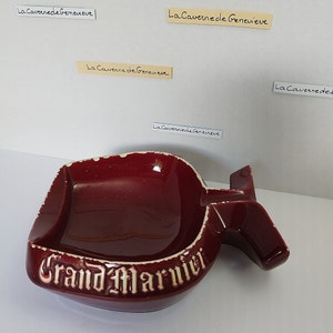 May include: A red ceramic ashtray shaped like a bottle with the words "Grand Marnier" in white lettering.