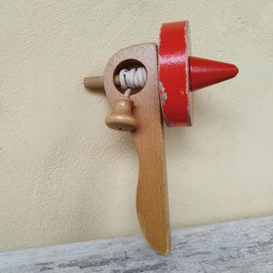 May include: A wooden spinning top with a red top and a wooden handle. The top has a string wrapped around it.