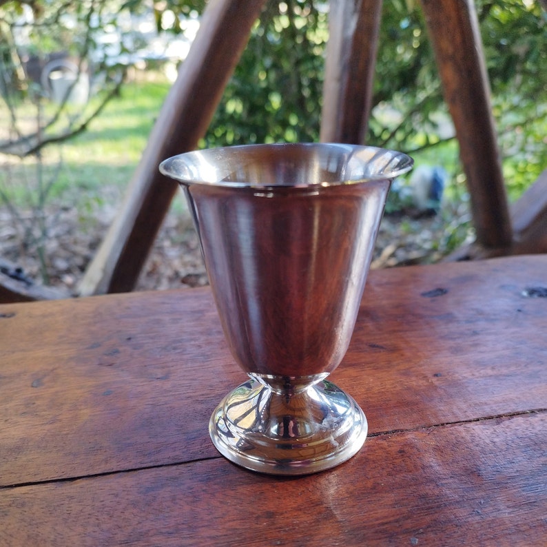May include: A silver metal goblet with a round base and a smooth, polished finish.